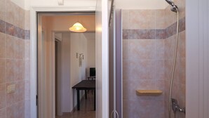 A bathroom with a shower, a toilet, and a sink. There is a door leading to a hallway with a table and chairs. - Villetta Torre Suda 1 (Racale)