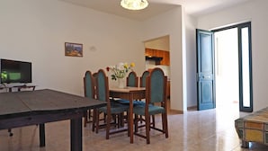 A dining area with a table, chairs, a vase of flowers, and a television on a stand. - Villetta Torre Suda 1 (Racale)