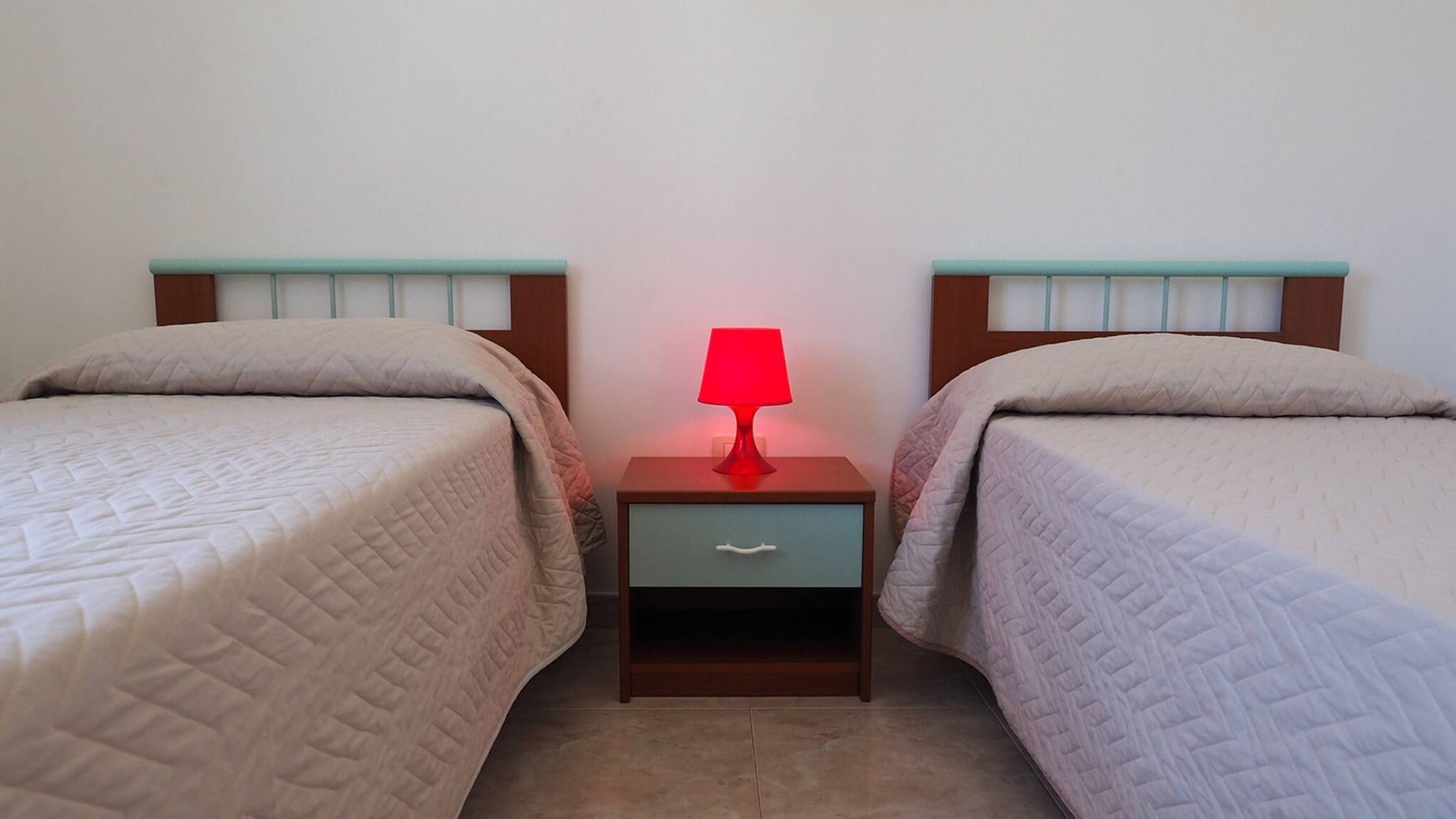 A twin room with two beds, each with a headboard and a bedside table with a lamp.