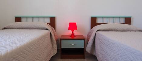 A twin room with two beds, each with a headboard and a bedside table with a lamp.