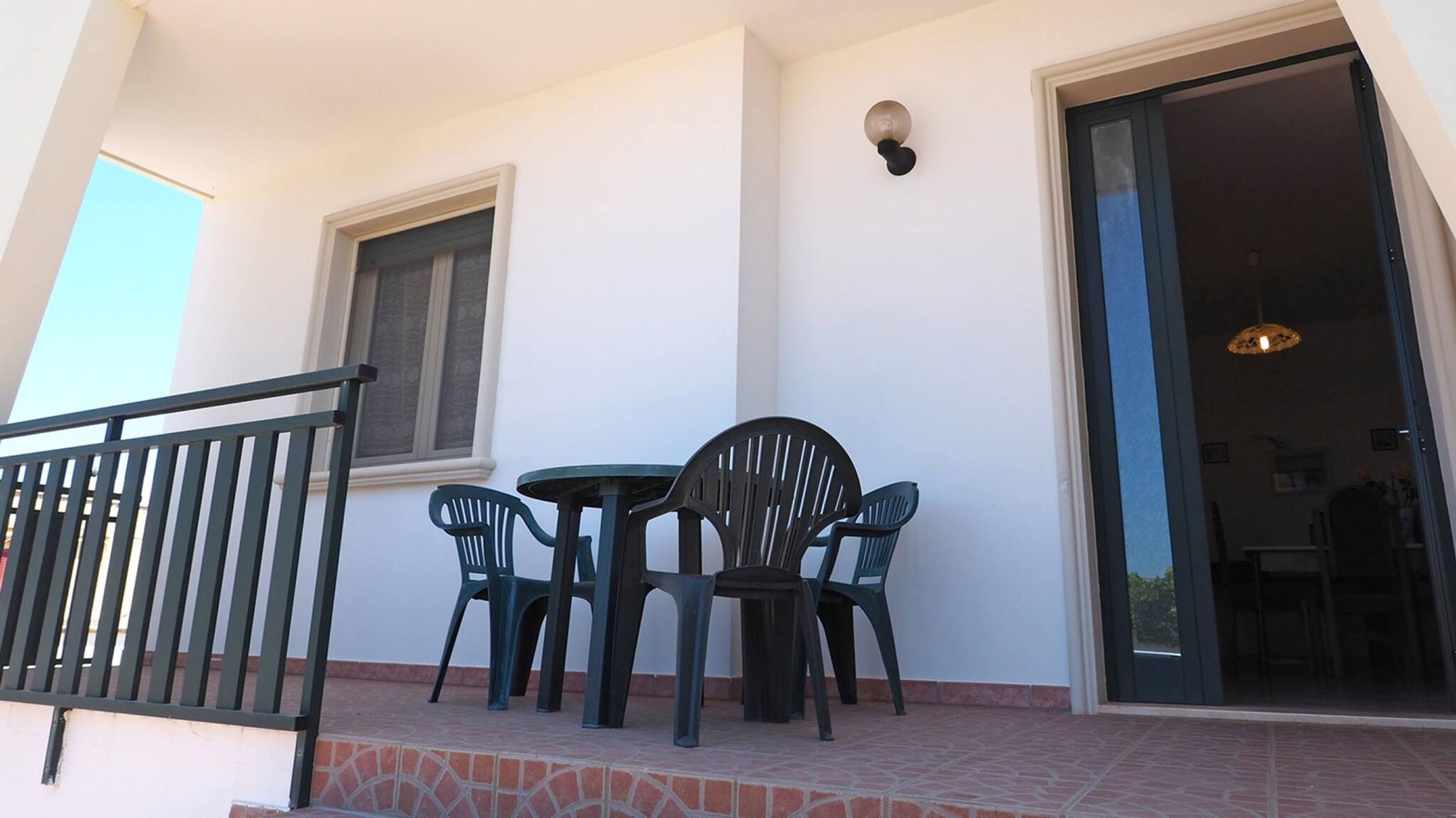 Ein Balkon mit Tisch und Stühlen, einem Fenster und einer Tür zu einem Innenraum.