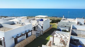 A coastal residential area with white buildings, a clear view of the sea, and a small green lawn. - Villetta Charme 2 in Capilungo 5 Guests by the sea (Alliste)