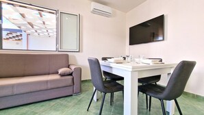 En moderne stue med en sofa, et spisebord med stole, et fladskærms-tv og en aircondition.