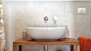 A bathroom with a large white vessel sink, a wooden vanity, and a towel rack with an orange towel. - Tenuta Alle Macchie in Racale (Racale)