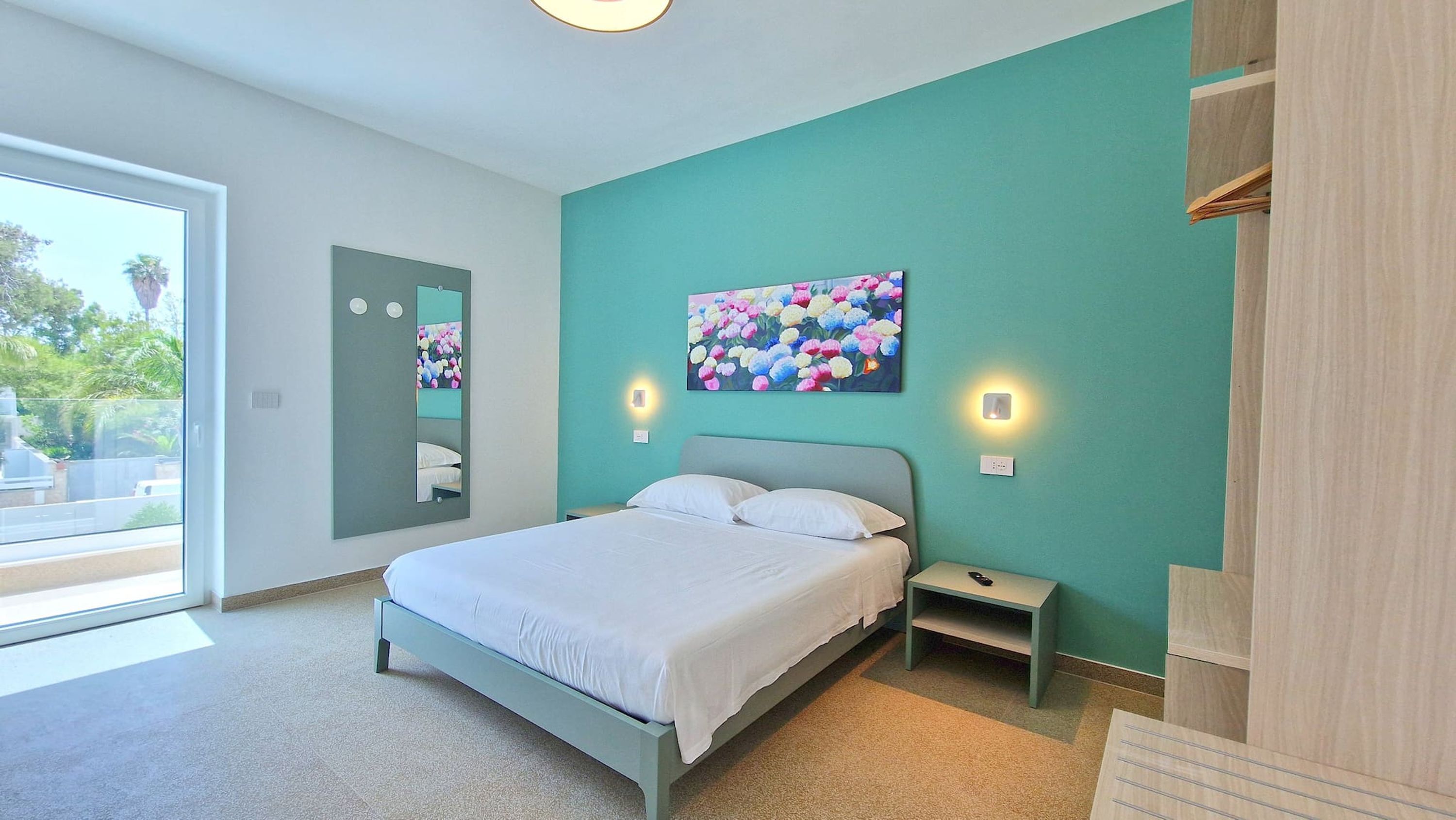 A modern bedroom with a bed, bedside tables, a mirror, and a painting.