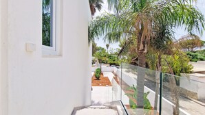 A modern building with a white exterior, a glass railing, and a view of a garden with palm trees and a pathway. - Suite Fontanelle Luxury 6 (Ugento)
