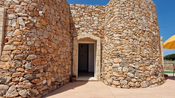 A stone building with a central doorway, a small window, and a potted plant. - Trullo Meraviglia in Torre Suda (Racale)