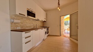 A compact kitchen with white cabinets, a wooden countertop, a built-in oven, a washing machine, and a tiled backsplash. - Trullo Meraviglia in Torre Suda (Racale)