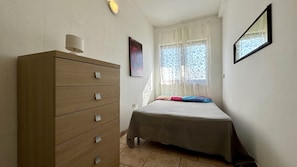 A bedroom with a wooden dresser, a bed with a grey bedspread, a window with sheer curtains, and a wall-mounted mirror. - Villetta Certosina 1 (Alliste)