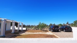 A white building with a covered patio area and two parked cars. - Villetta Certosina 1 (Alliste)