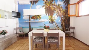 Un comedor con una mesa y sillas, un mural decorativo con escena de playa, y un aire acondicionado montado.