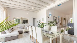 Una sala de estar moderna con una mesa de comedor de vidrio, sofás blancos y un espejo grande.