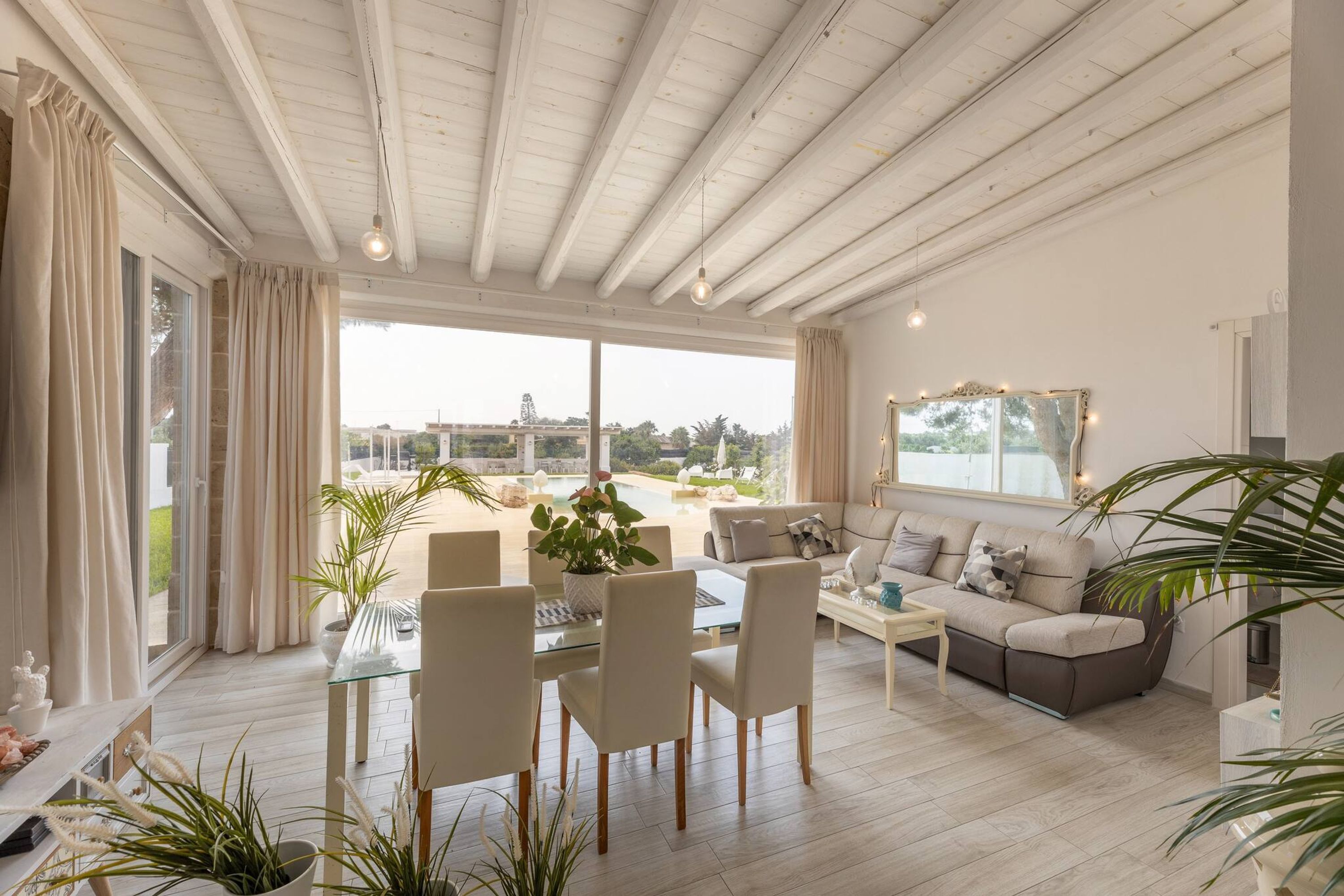 En rummelig stue med et glasbord, beige sofaer og et spiseområde med stole og et bord af glas.