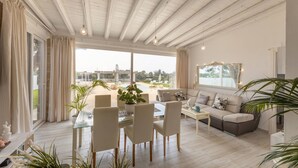 Amplia sala de estar con una mesa de centro de vidrio, sofás color beige y un comedor con sillas y una mesa de vidrio.