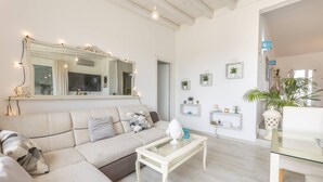 Una sala moderna con un sofá seccional color beige, una mesa de centro de vidrio y un espejo grande sobre el sofá. Hay pequeñas repisas con objetos decorativos en la pared.