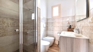 Un baño moderno con cabina de ducha de vidrio, inodoro y lavamanos con espejo.