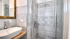 Un baño con lavamanos blanco, un espejo y una ducha con azulejos estampados.