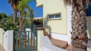 A residential building with a white exterior, a green gate, and a staircase leading to the entrance. - Appartamento Torre Suda 2 (Racale)