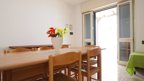 A dining area with a wooden table, chairs, and a white vase with flowers. - Appartamento Torre Suda 2 (Racale)