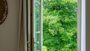 Une porte ouverte donne sur un jardin luxuriant et verdoyant, où l’on aperçoit une plante en pot et un cactus sur le seuil.