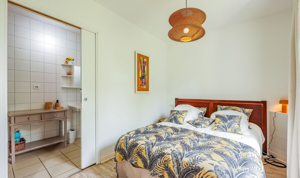 Ein Schlafzimmer mit Bett, Nachttisch, Pendelleuchte und einem an der Wand hängenden Bild.