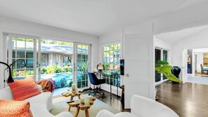 A spacious living room with a large window, a pool, and a dining area with a table and chairs. - 3BR secluded gem w/ pool, minutes to beaches/marinas, walk to town & restaurants (Hampton Bays)