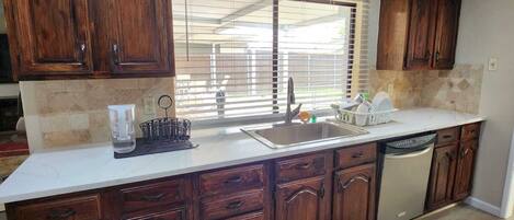 A kitchen with wooden cabinets, a sink, and a window with blinds.