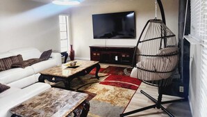 Una sala de estar con un sofá blanco, una mesa de centro, un sillón colgante, un televisor y una chimenea.