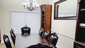 Comedor con una amplia mesa de madera, sillas tapizadas en negro, una lámpara de araña y una estantería de madera.