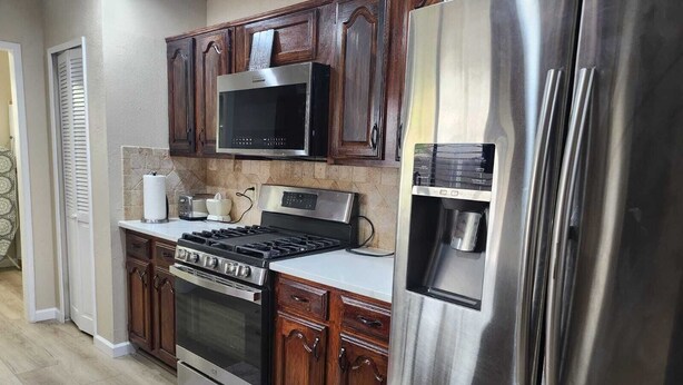 Una cocina con un refrigerador de acero inoxidable, un microondas, una estufa y armarios de madera.