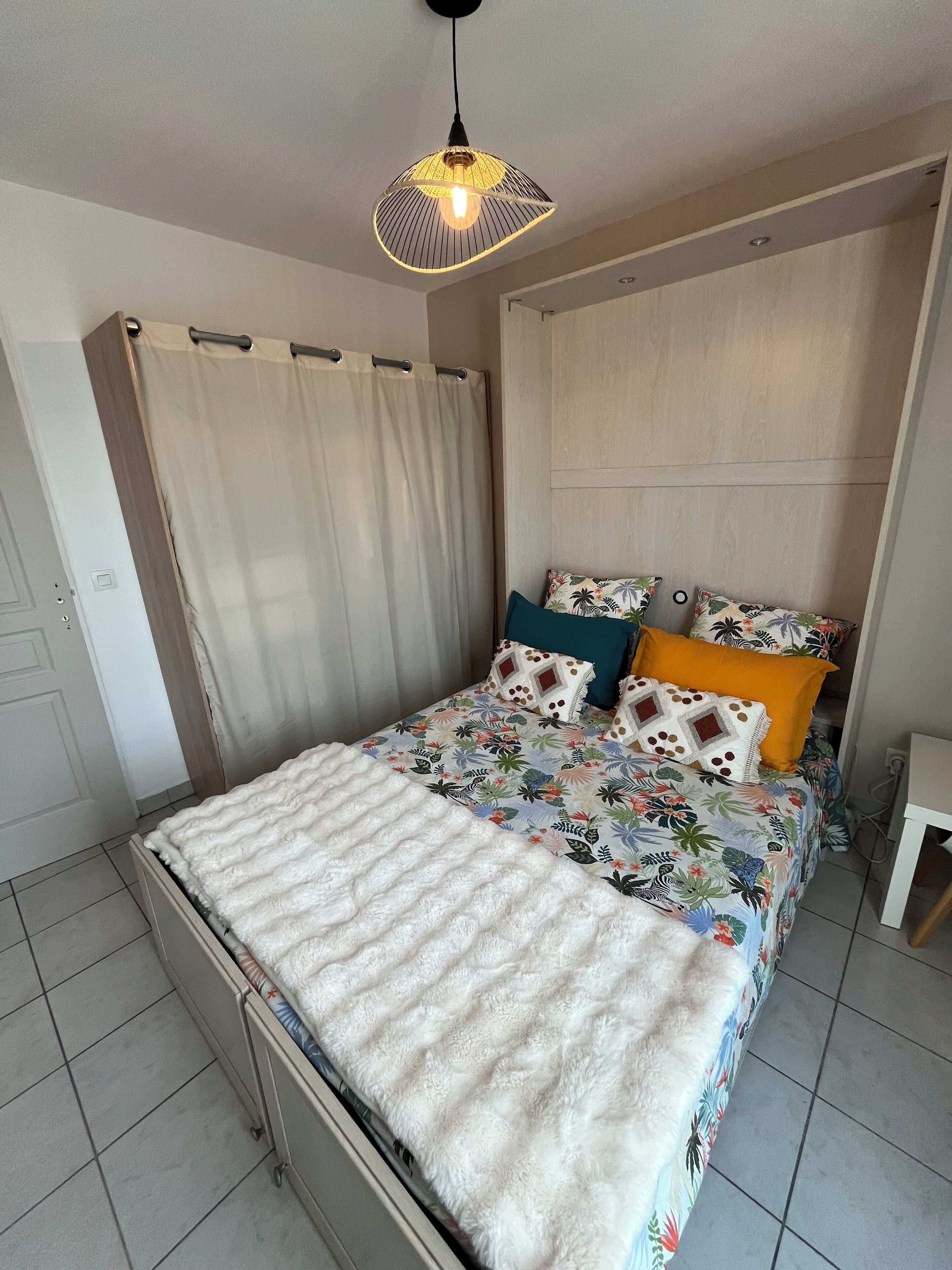 A neatly made bed with a floral bedspread, a white fluffy blanket, and a variety of pillows.