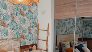 A bedroom with a bed, a nightstand, a mirror, and a wall with a tropical leaf pattern.