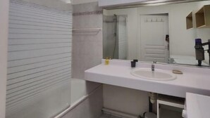 A modern bathroom with a white sink, mirror, and toilet. There is a towel rack and a small trash bin.