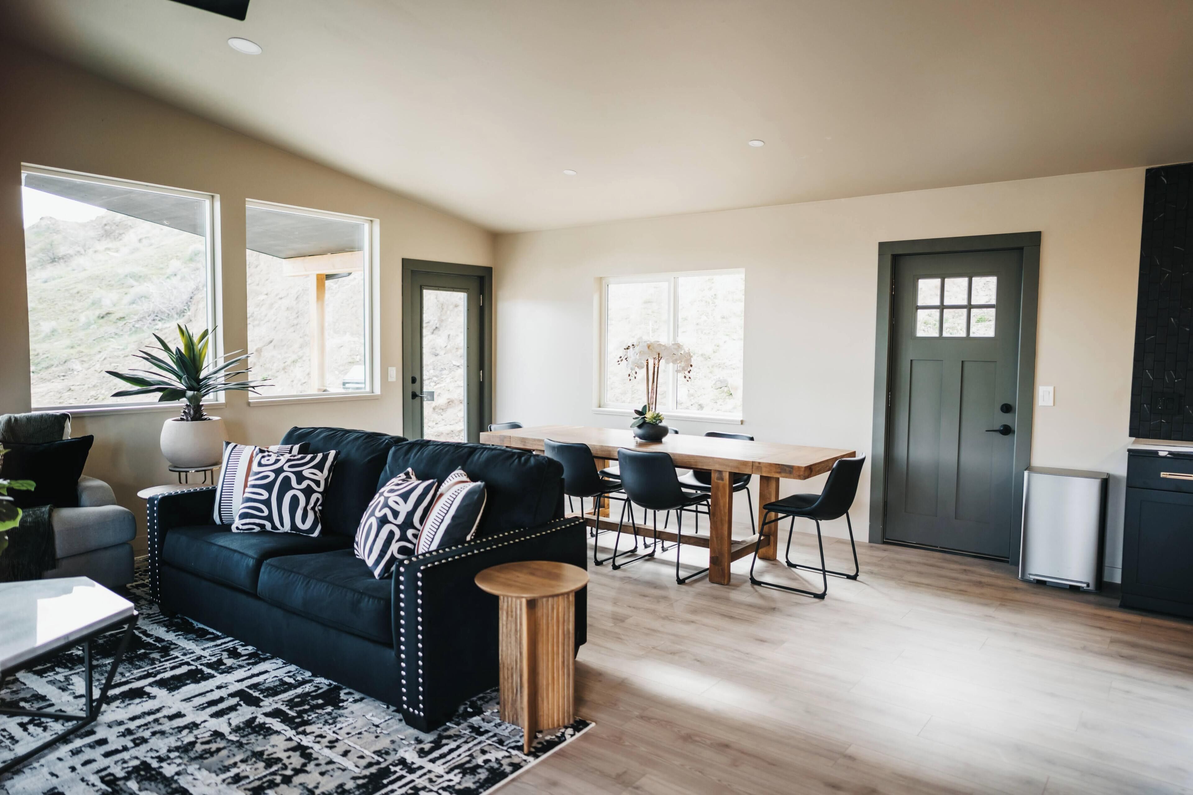 A modern living room with a black sofa, a dining table, and a kitchen area.