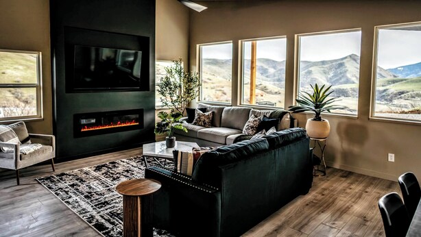Una sala moderna con chimenea, un sofá, una mesa de centro y ventanas amplias con vistas a las montañas.