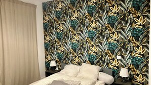 Ein Schlafzimmer mit einem Bett, zwei Nachttischen mit Lampen, einem Vorhang und einer Wand mit einem Blattmuster.