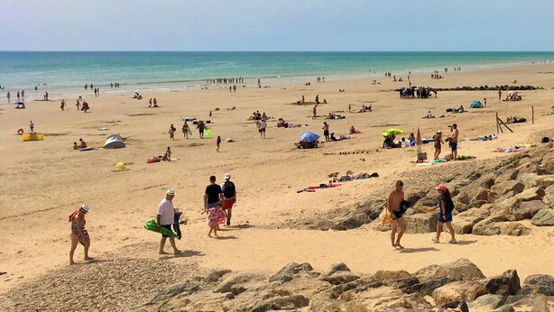 Ein Strand mit Menschen, die spazieren gehen und sonnenbaden, Zelten und Sonnenschirmen.