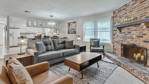 A modern living room with a fireplace, a sofa, a coffee table, and a kitchen in the background. - Cozy 3BR townhome 5 minutes from downtown and Cascades (Tallahassee)