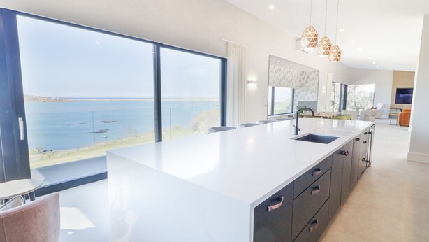 A modern kitchen with a large island, a view of the sea, and pendant lighting. - Atlantic Sea Breeze (Killult)