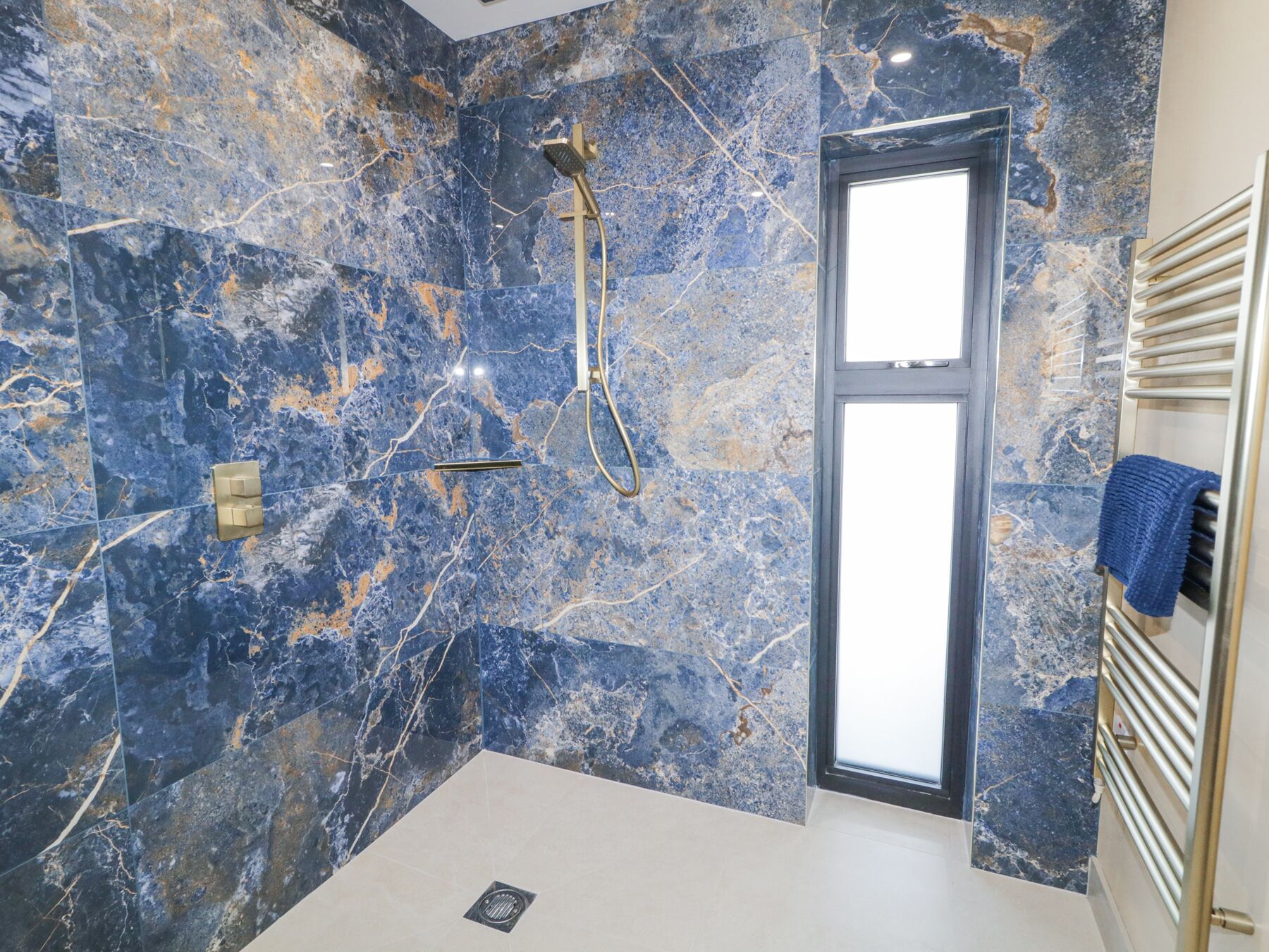 Un baño con ducha, paredes de mármol, un perchero y una puerta.