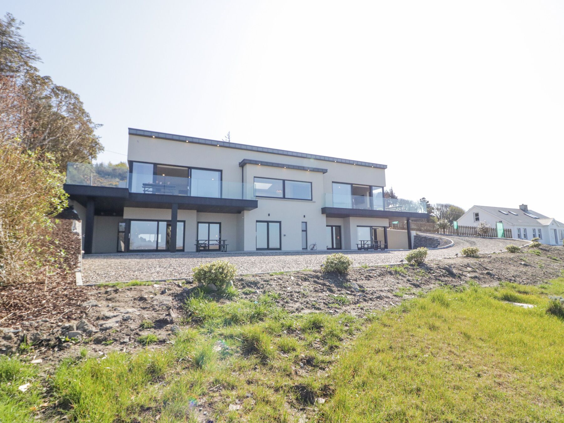 A modern two-story house with a flat roof, large windows, and a balcony.