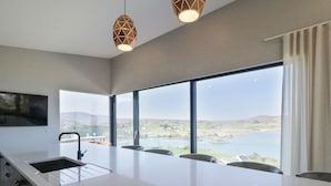 A modern kitchen with a large island, a built-in sink, and a view of a lake and hills. - Atlantic Sea Breeze (Killult)