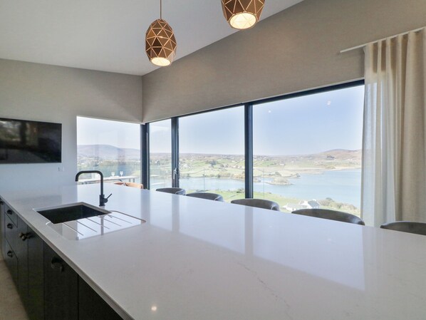 A modern kitchen with a large island, a built-in sink, and a view of a lake and hills.
