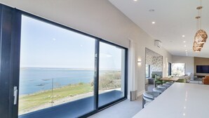 A modern interior with large windows offering a view of the sea and a dining area with a white table and chairs. - Atlantic Sea Breeze (Killult)