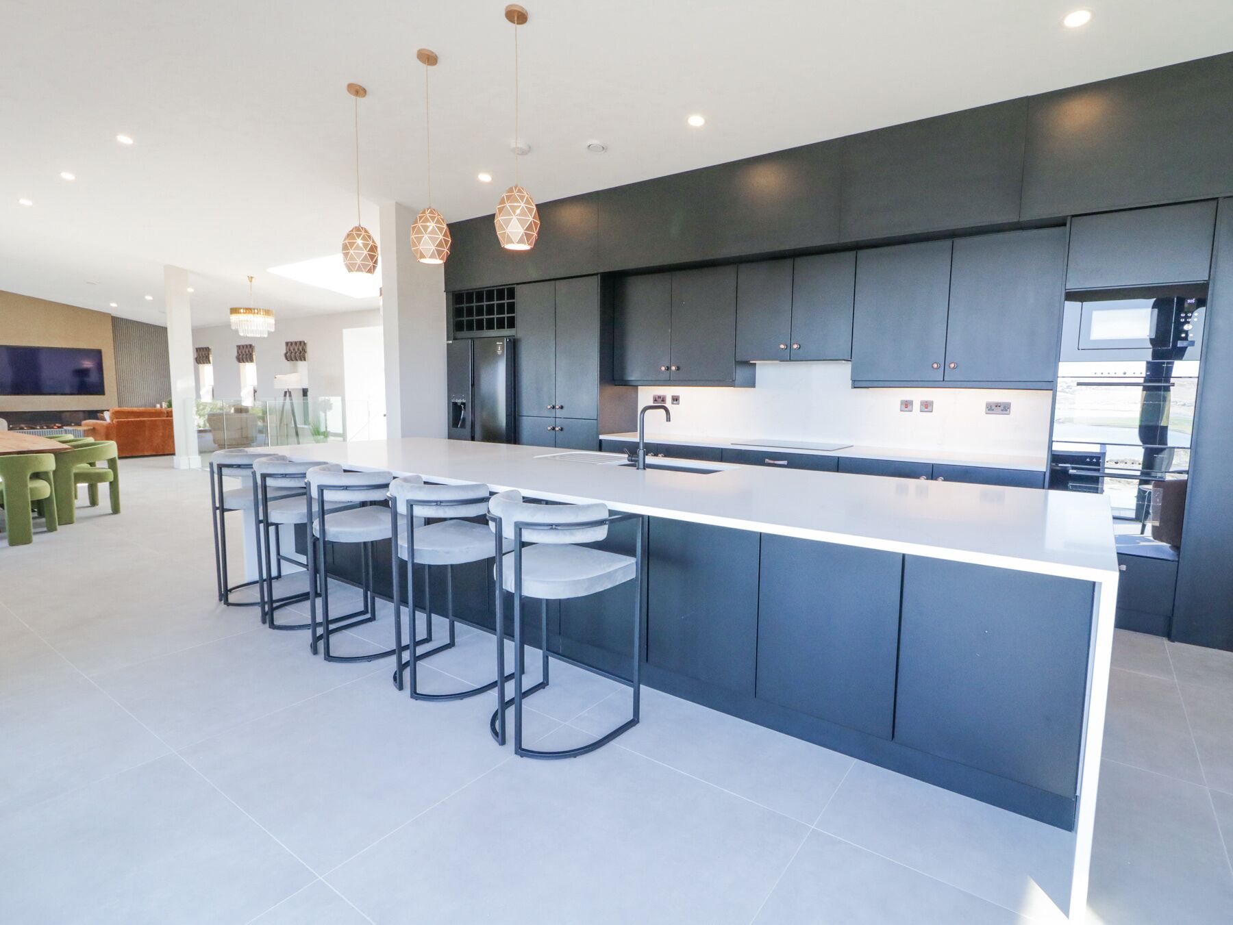 A modern kitchen with a large island, bar stools, dark cabinetry, and pendant lighting.