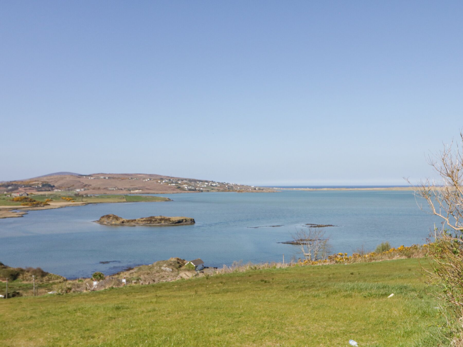 A coastal landscape with a clear view of the sea, grassy areas, and distant hills.