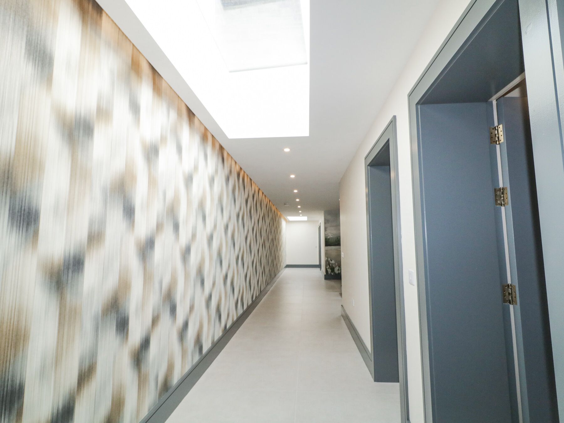A modern hallway with a patterned wall, a skylight, and a door with a metal handle.