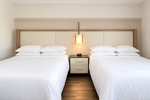 A hotel room with two beds, a nightstand with a lamp, and a wooden floor.