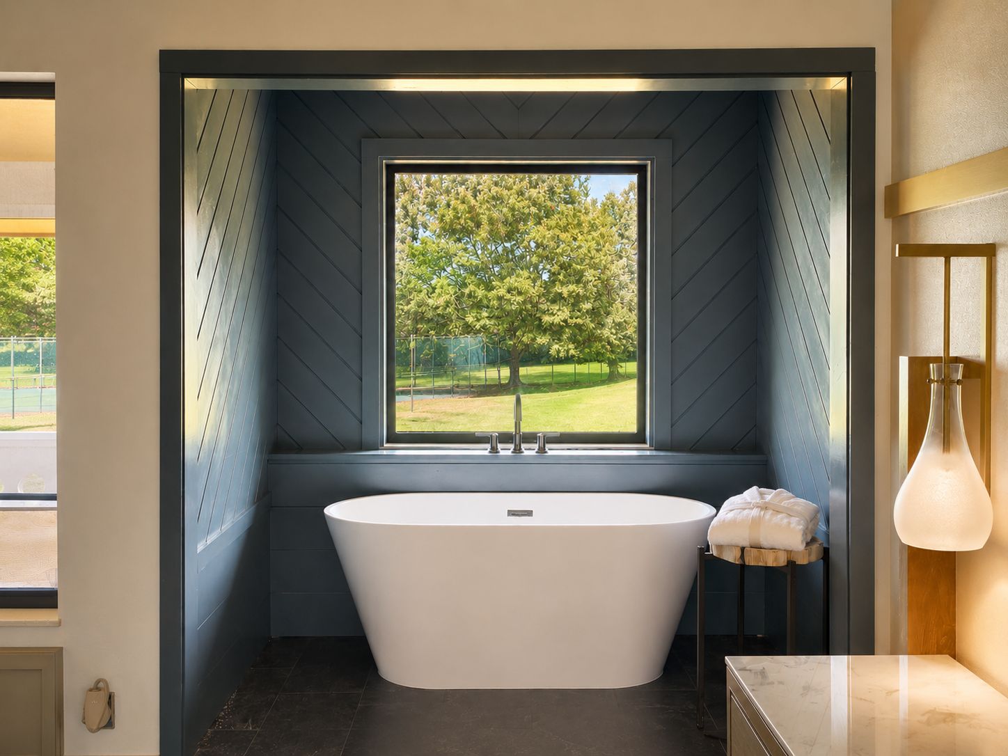 A modern bathroom with a freestanding bathtub, a window with a view of greenery, and a minimalist design.