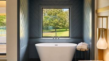 A modern bathroom with a freestanding bathtub, a window with a view of greenery, and a minimalist design.